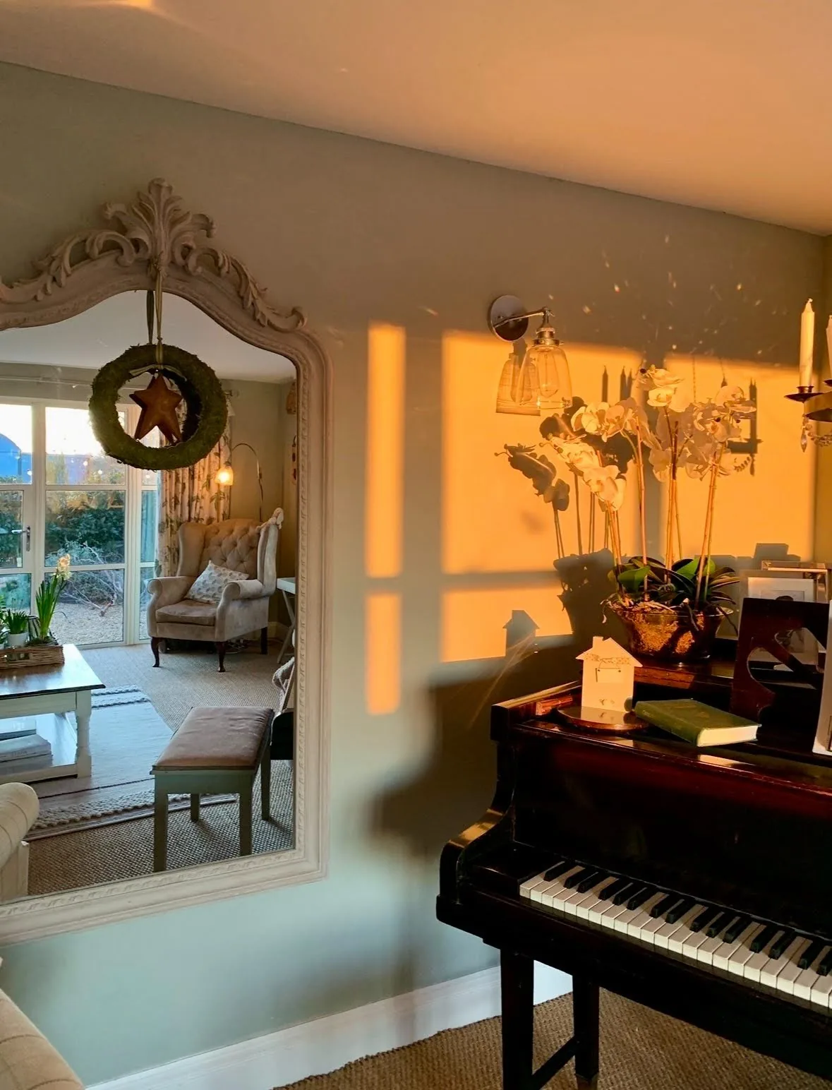 Late golden-hour light falling across a piano dressed with white orchids, candles and a carved mirror