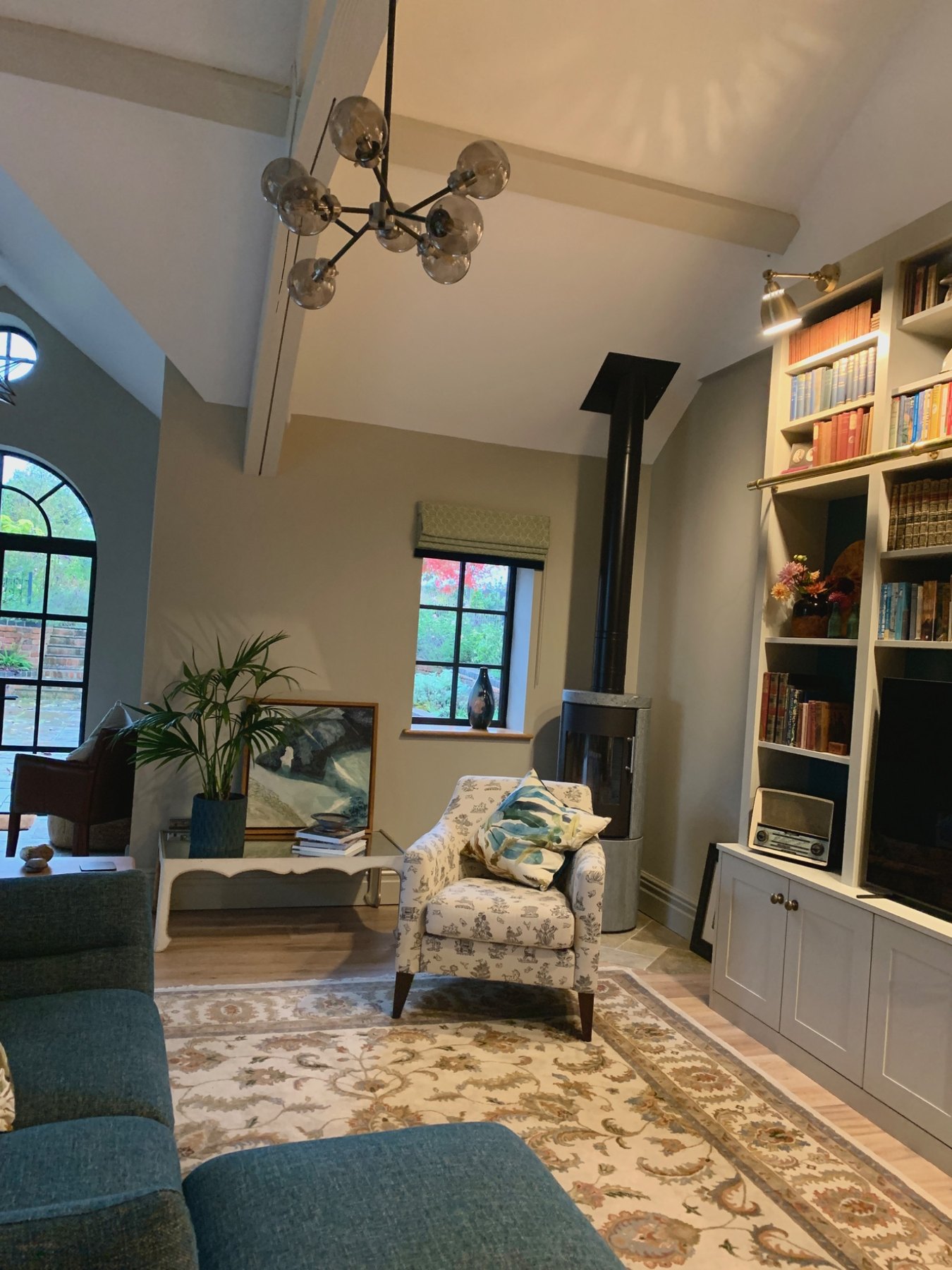 Period property sitting room with log burner, chandelier, arched window and beamed ceiling