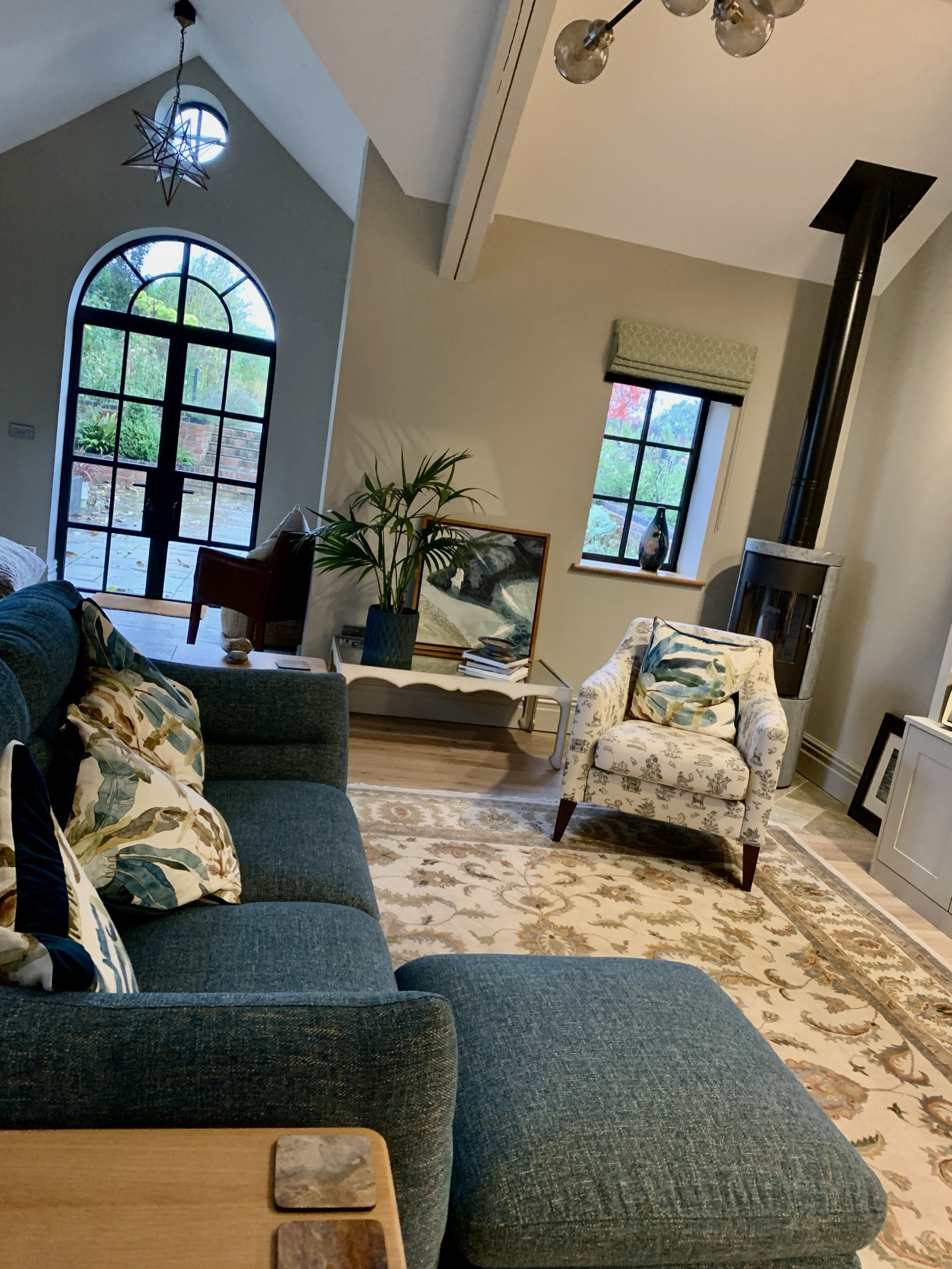 The Apple Loft — period barn conversion living room with vaulted ceiling, arched window, teal sofa, and log burner