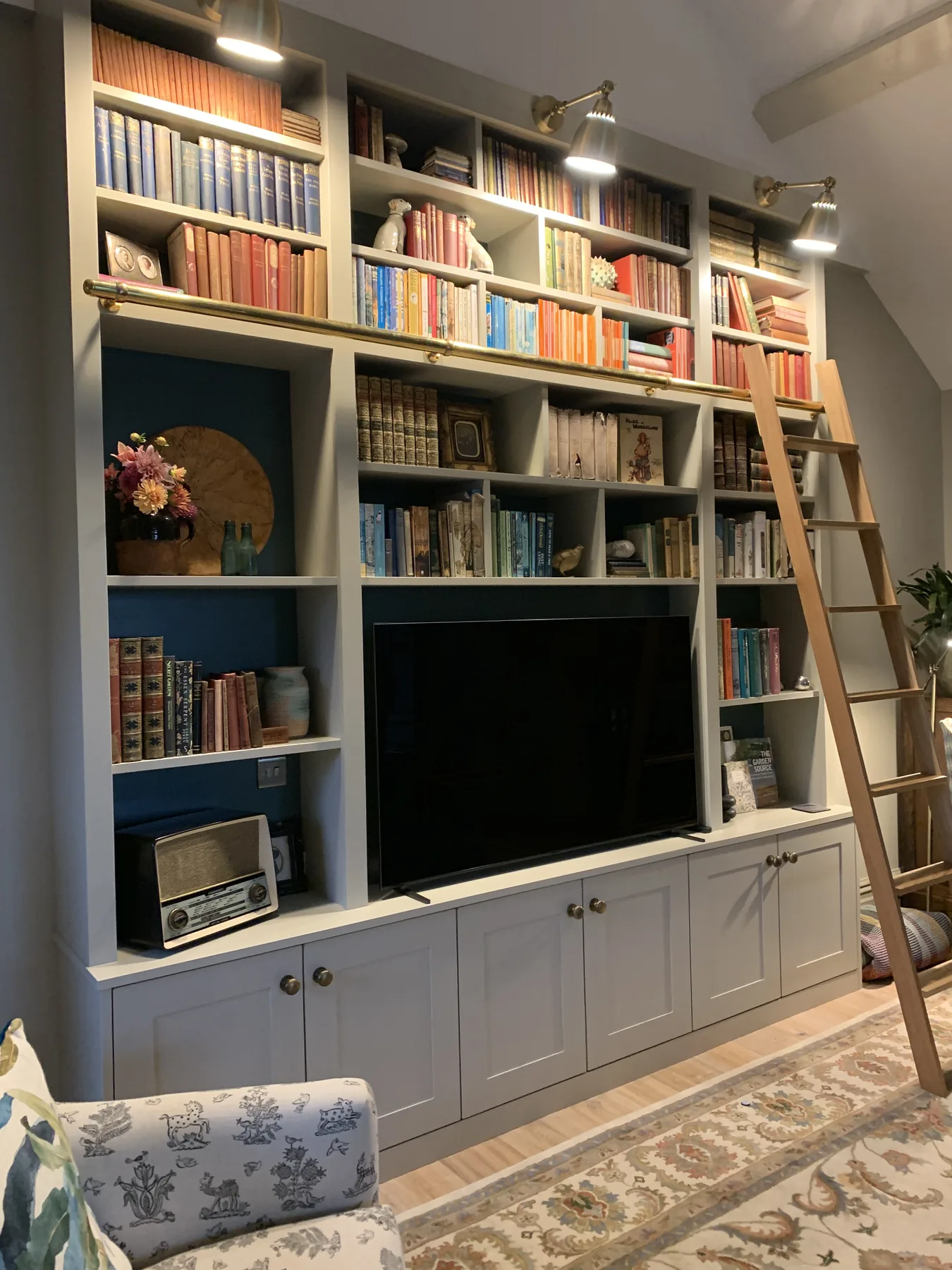 Open-plan living with bespoke bookshelf wall, library ladder, log burner, and arched garden window