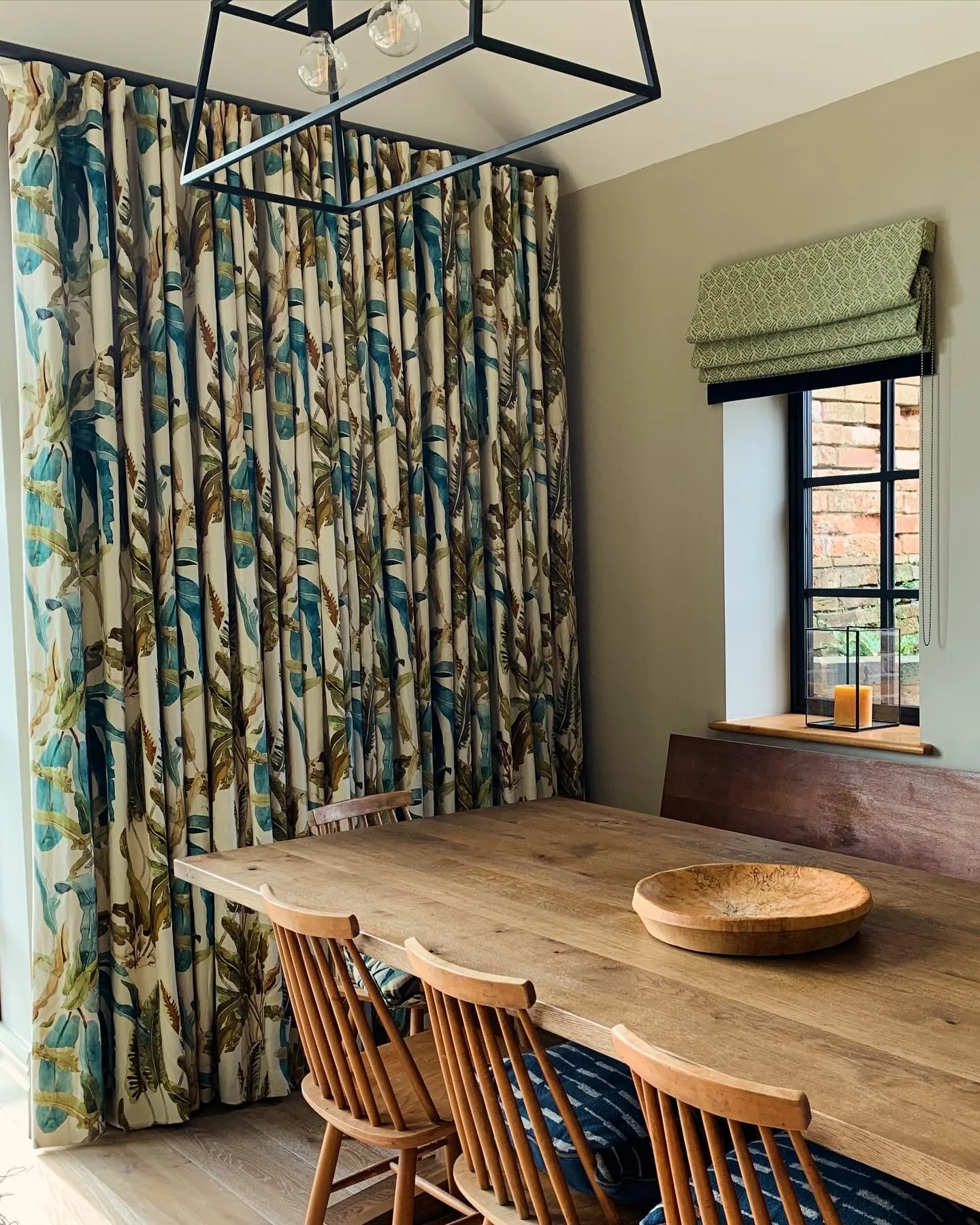 Dining area with botanical-print curtains, oak refectory table, and spindleback chairs