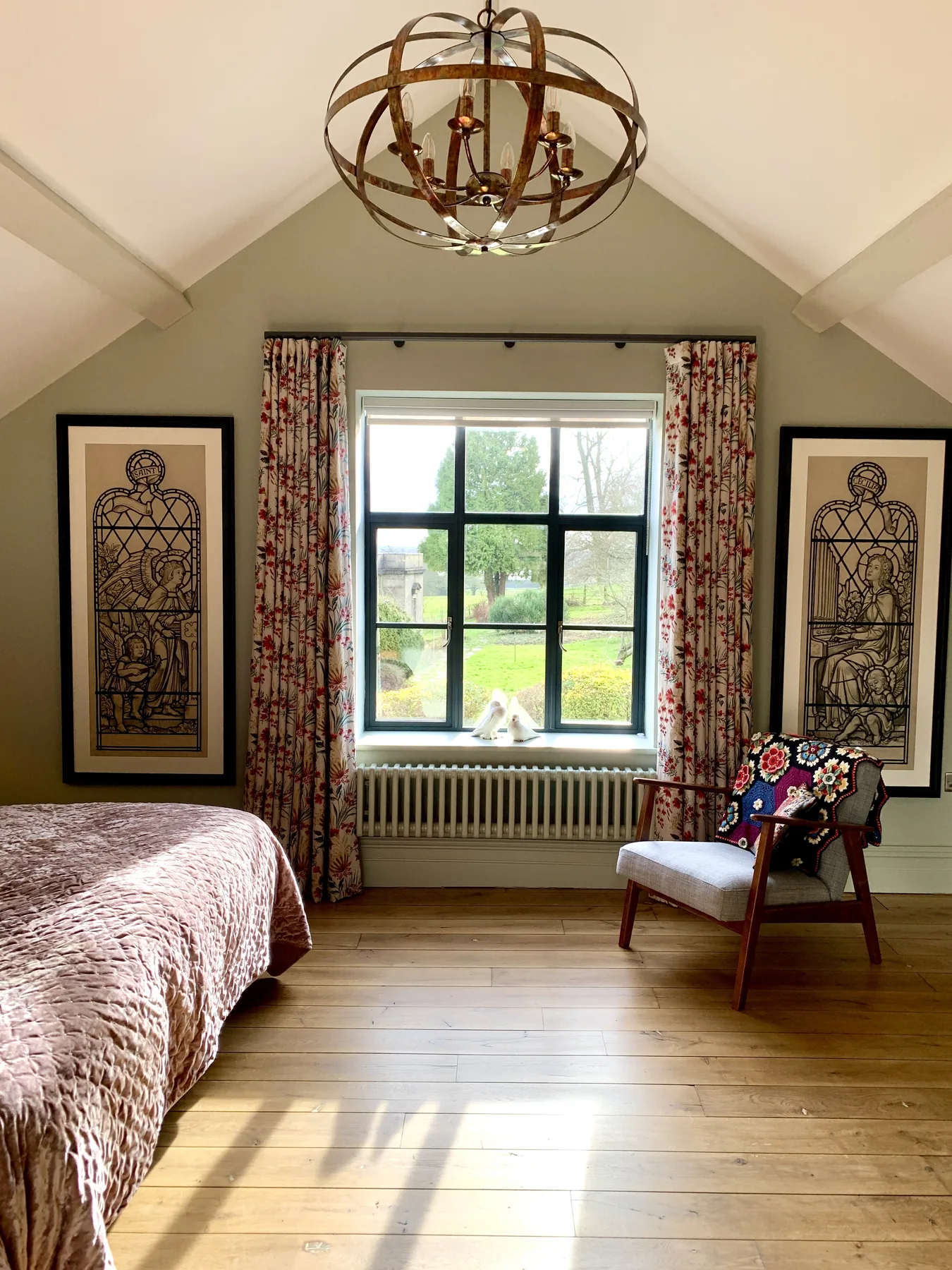 Bedroom with vaulted ceiling, ecclesiastical artworks, floral curtains, and orb chandelier