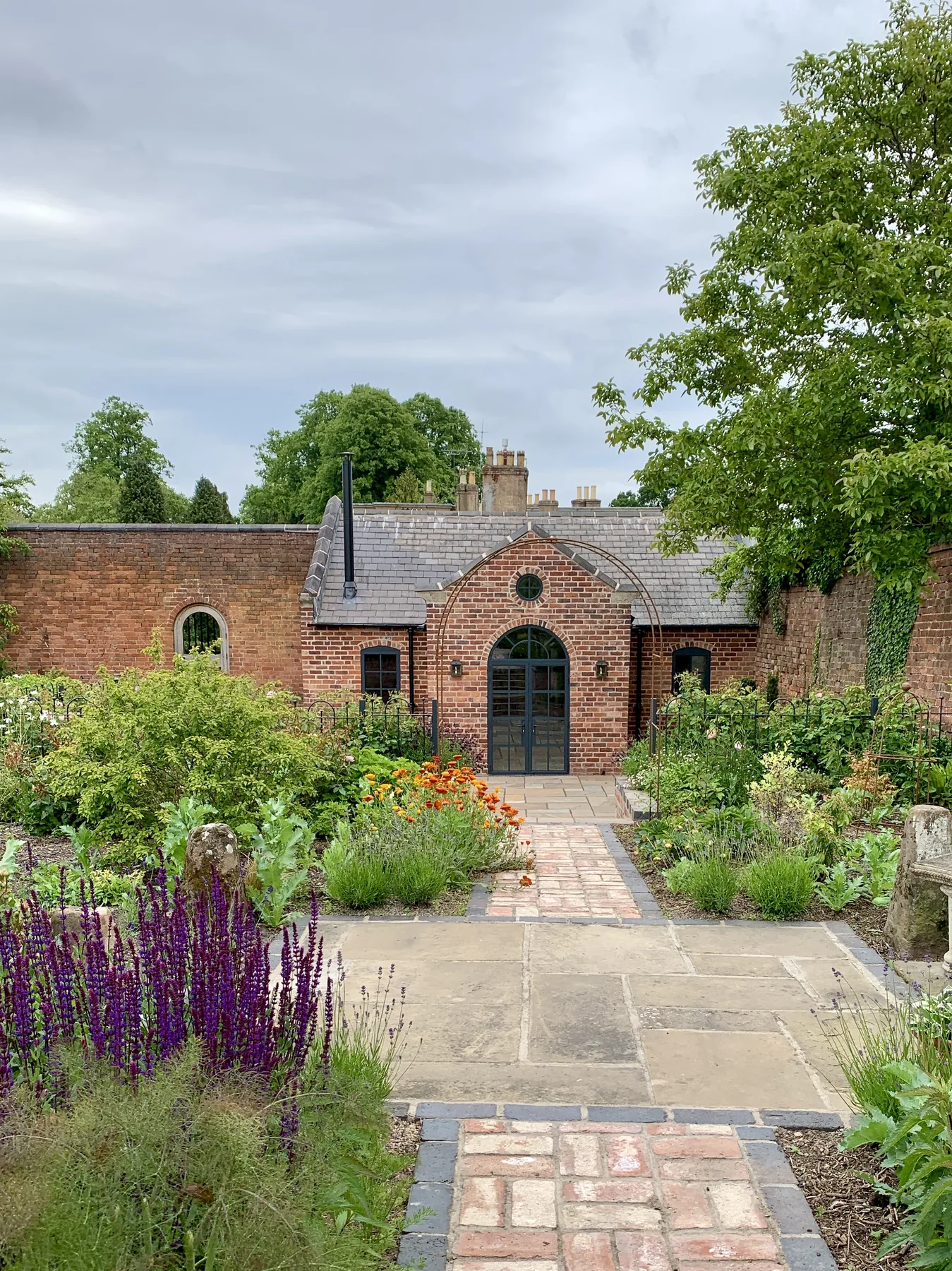 The walled garden approach to the converted barn — arched glazed doors, brick path, and lavender beds
