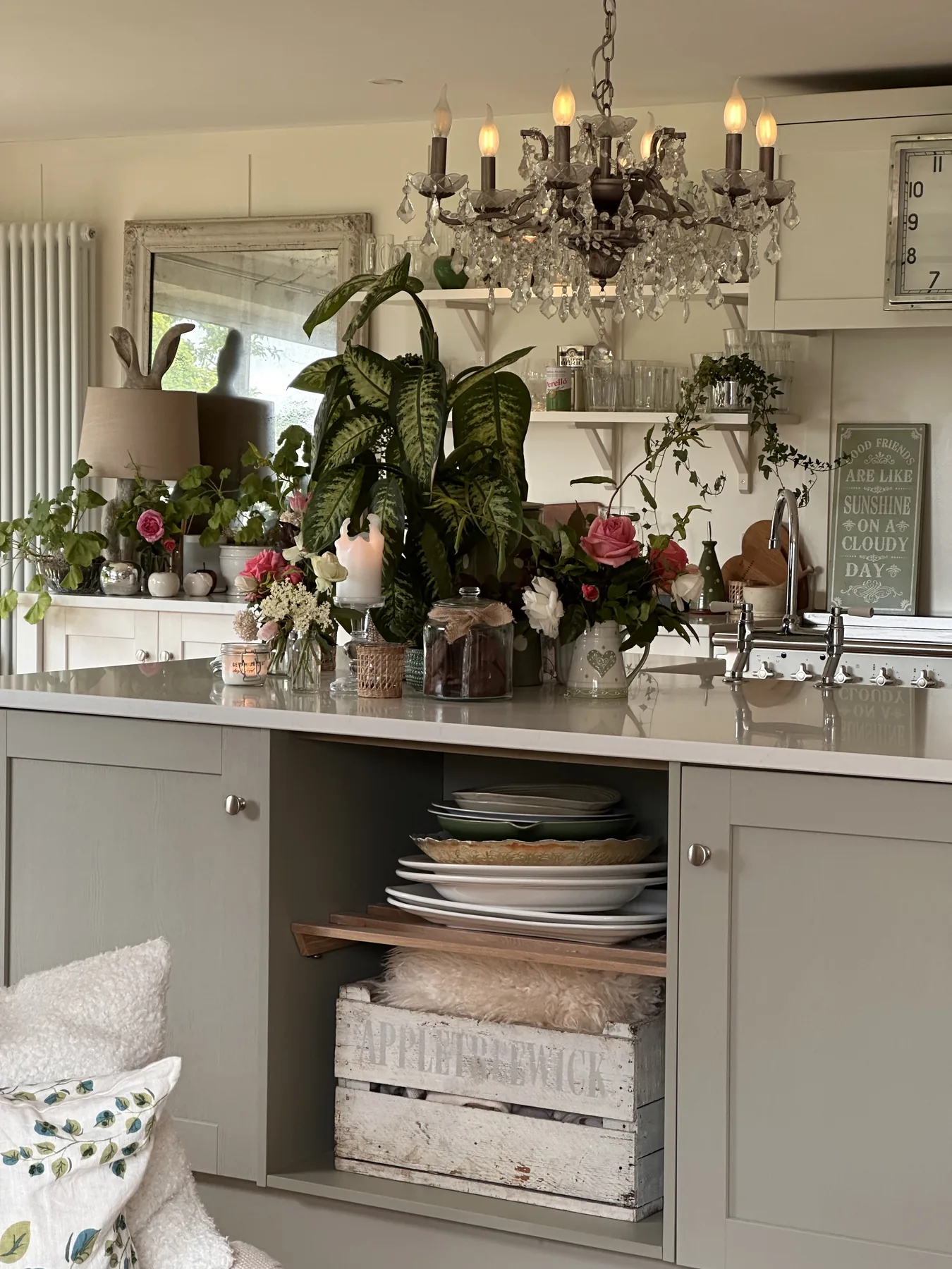 Chandelier above a styled console — fresh roses, candlelight, antique mirror, and a curated dresser of plates and ceramics