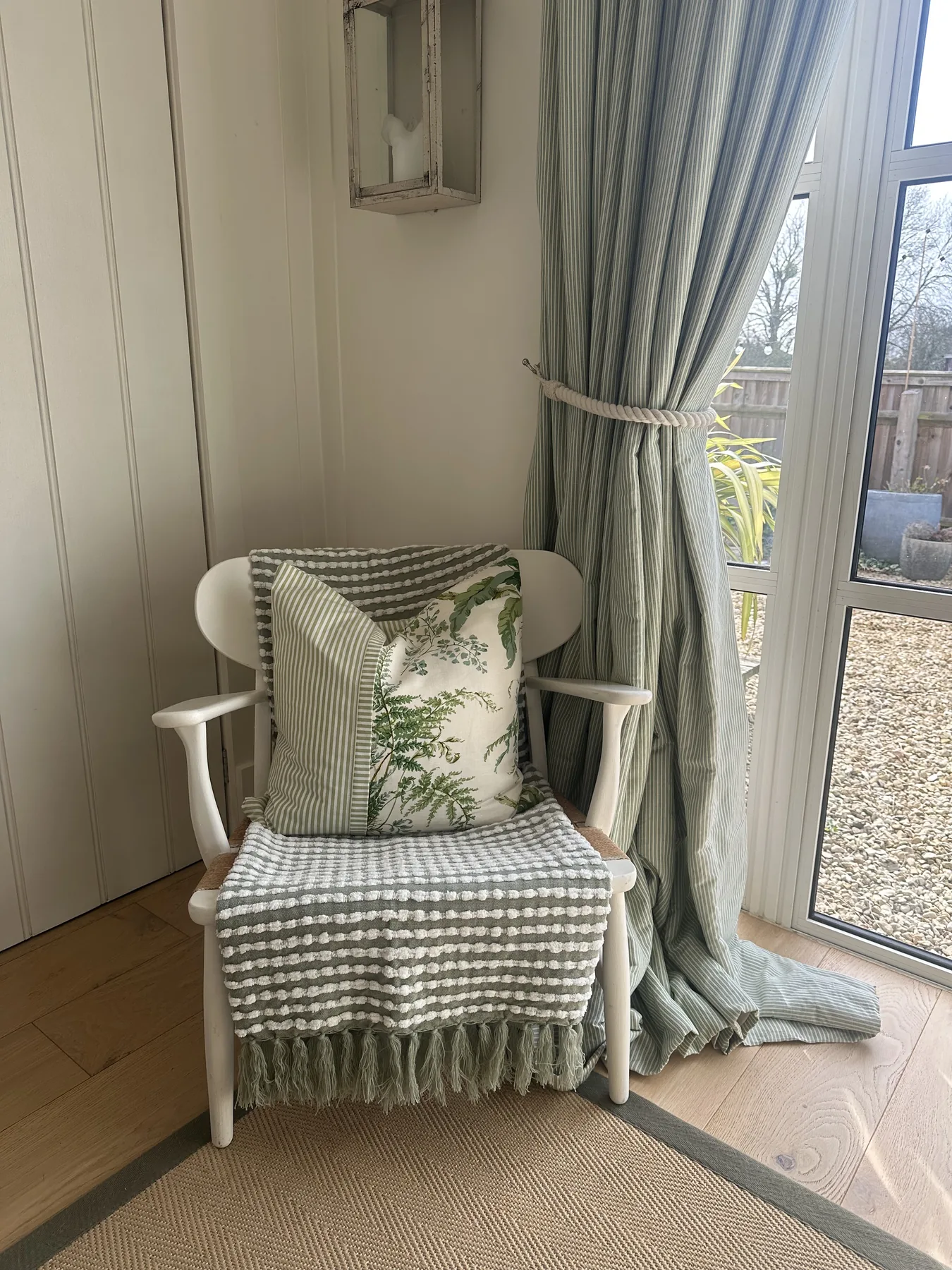 A painted spindle chair dressed with botanical and striped cushions beside French doors to the garden
