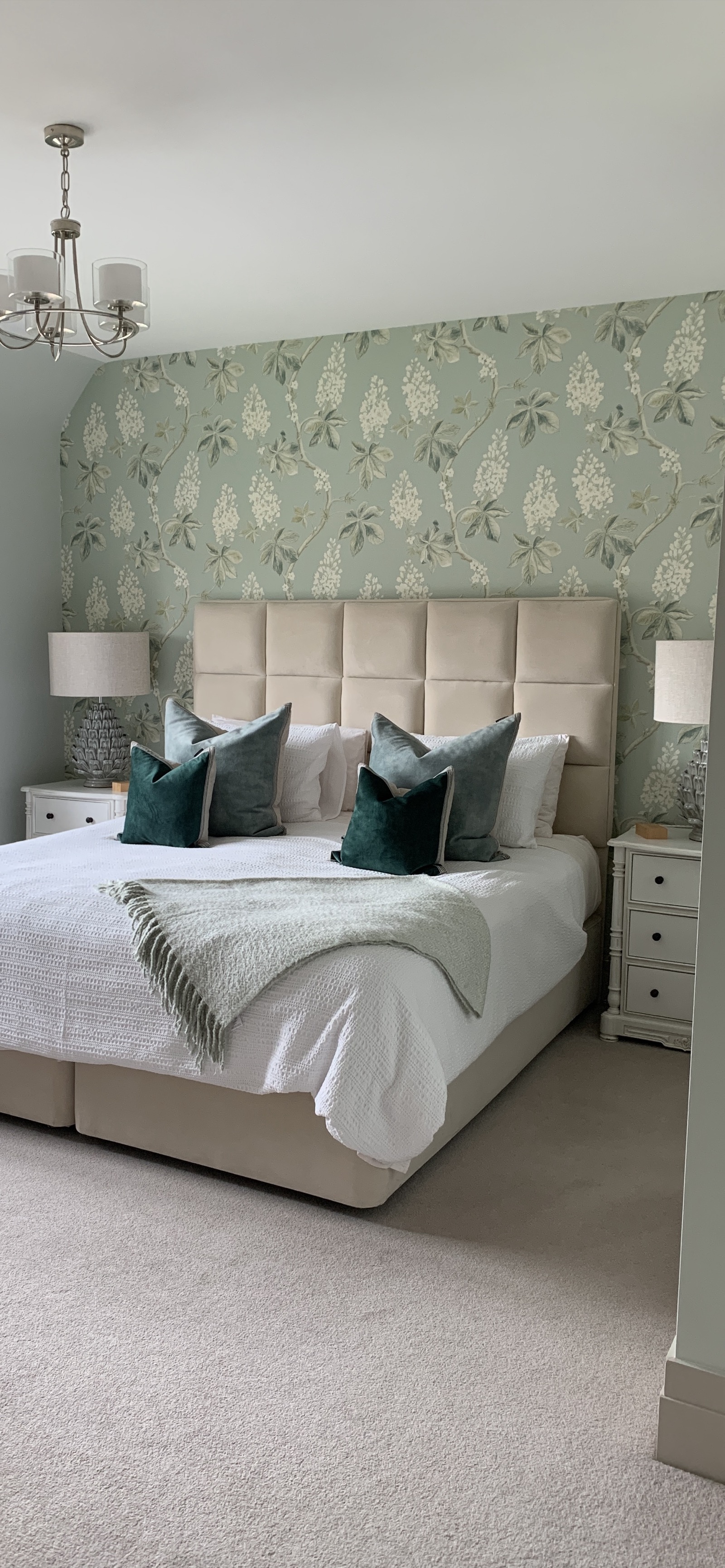 Master bedroom with teal velvet cushions, floral wallpaper, and symmetrical styling